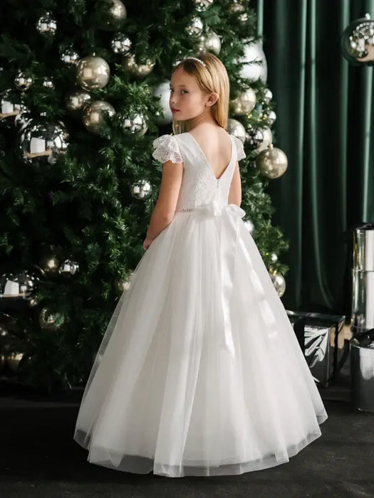 Teter Warm Julia off-white lace communion dress worn by a girl standing beside a decorated Christmas tree.