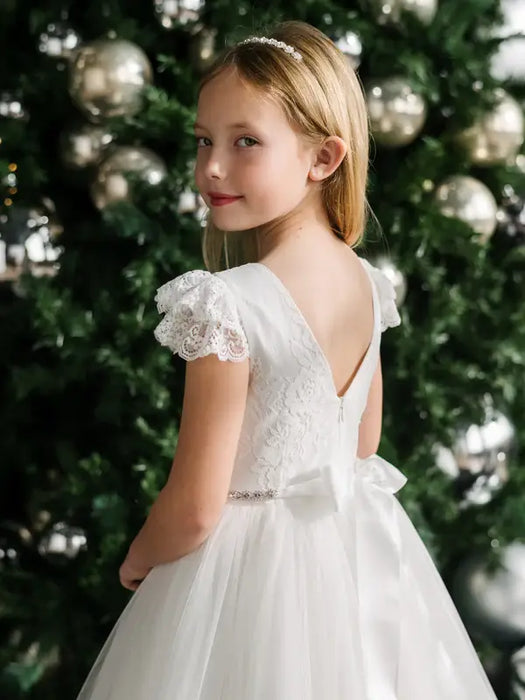 Teter Warm Julia off-white lace communion dress worn by a girl standing in front of a decorated tree.