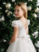 Teter Warm Julia off-white lace communion dress worn by a girl standing in front of a decorated tree.