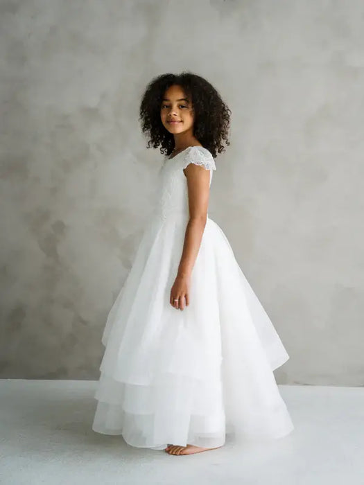 Teter Warm Lenni off-white communion dress worn by a girl standing sideways against a neutral background.