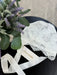 Teter Warm Leslie Lace Baby Bonnet displayed on a dark surface with white ribbons and flowers nearby.