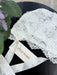 Teter Warm Leslie lace baby bonnet in white shown resting on a flat black surface with ribbon ties.