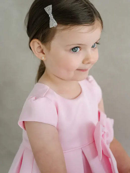 Teter Warm Lettie Pink Party Dress shown on a young girl with a jeweled hair bow, side view.