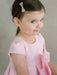 Teter Warm Lettie Pink Party Dress shown on a young girl with a jeweled hair bow, side view.