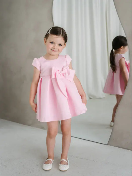 Teter Warm Lettie pink party dress on a young girl standing indoors with a large bow detail.