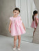 Teter Warm Lettie pink party dress on a young girl standing indoors with a large bow detail.