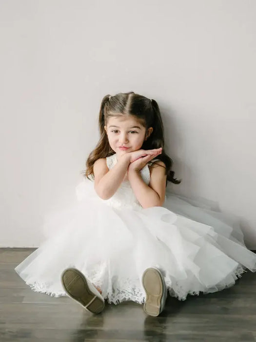 Teter Warm May off white lace flower girl dress worn by a young girl sitting on a floor indoors.