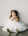 Teter Warm May off white lace flower girl dress worn by a young girl sitting on a floor indoors.