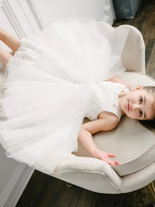 Teter Warm off-white lace flower girl dress worn by a child sitting on a light chair indoors.
