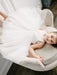 Teter Warm off-white lace flower girl dress worn by a child sitting on a light chair indoors.
