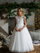 Teter Warm Nadia off-white lace communion dress worn by a girl standing in a cozy living room.