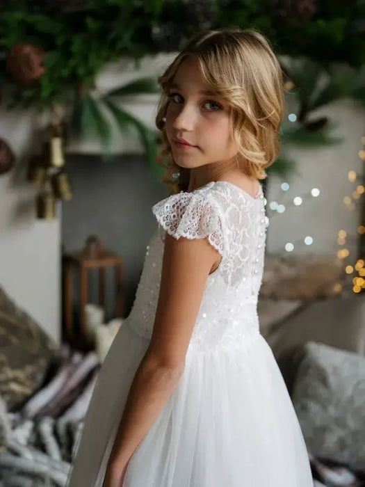Teter Warm Nadia off-white lace communion dress worn by a girl standing indoors near festive decor.