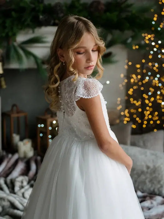 Teter Warm Nadia off-white lace communion dress shown on a girl in a softly lit room with festive decor.