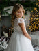 Teter Warm Nadia off-white lace communion dress shown on a girl in a softly lit room with festive decor.