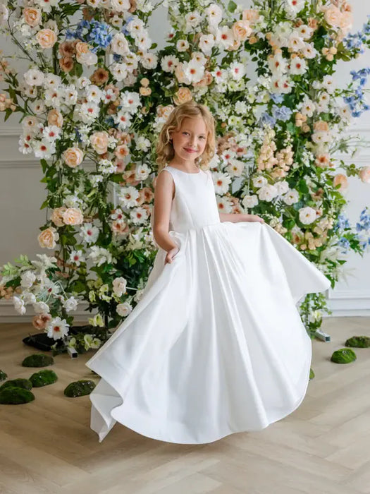 Teter Warm Penelope off-white communion dress worn by a girl standing in front of floral backdrop.