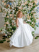 Teter Warm Penelope off-white communion dress worn by a girl standing in front of floral backdrop.