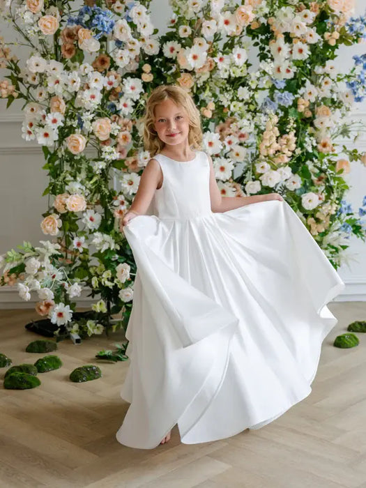 Teter Warm Penelope off white communion dress shown on a young girl in front of floral backdrop.