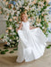 Teter Warm Penelope off white communion dress shown on a young girl in front of floral backdrop.