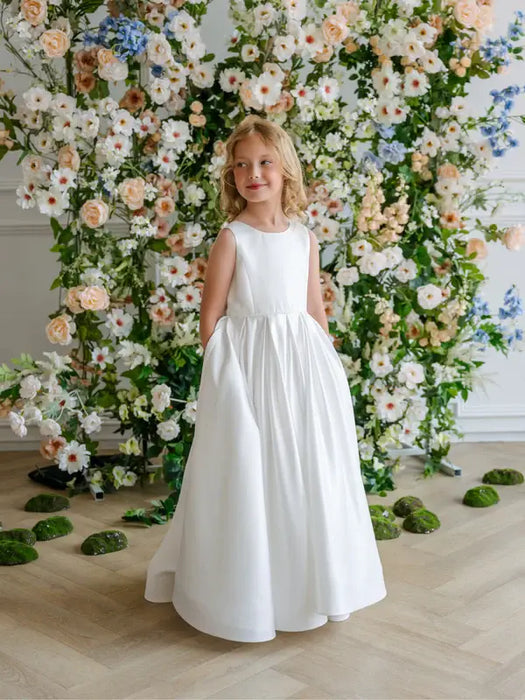 Teter Warm Penelope off-white communion dress shown on a young girl standing before a floral backdrop.
