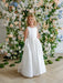 Teter Warm Penelope off-white communion dress shown on a young girl standing before a floral backdrop.