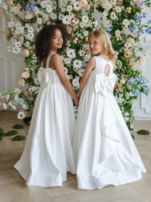 Teter Warm Penelope off-white communion dresses on two girls standing in front of floral backdrop.