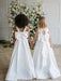Teter Warm Penelope off-white communion dresses with large bows, worn by two girls holding hands indoors.