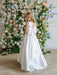 Teter Warm Penelope Off-White Communion Dress on girl with bow back, standing by floral backdrop.