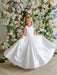 Teter Warm Penelope off-white communion dress worn by a girl twirling in front of floral backdrop.