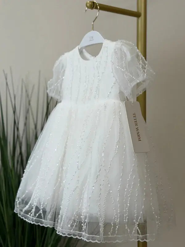 Teter Warm Perla off-white sequin baptism dress with short sleeves hanging on a gold rack.