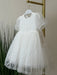 Teter Warm Perla off-white sequin baptism dress with short sleeves hanging on a gold rack.