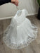 Teter Warm Perla off-white sequin baptism dress displayed on a hanger over a wood floor.