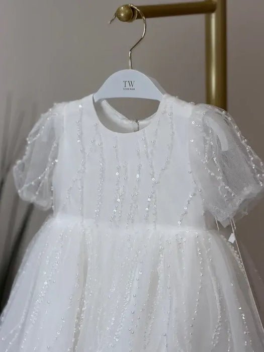 Teter Warm Perla off-white sequin baptism dress with sheer sleeves hanging on a rack.