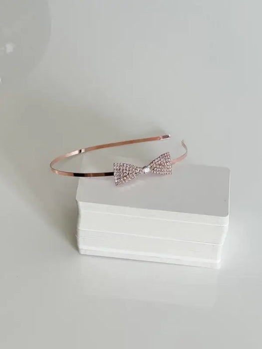 Teter Warm Polli rose gold headband with crystal bow displayed on a white box against a plain background.
