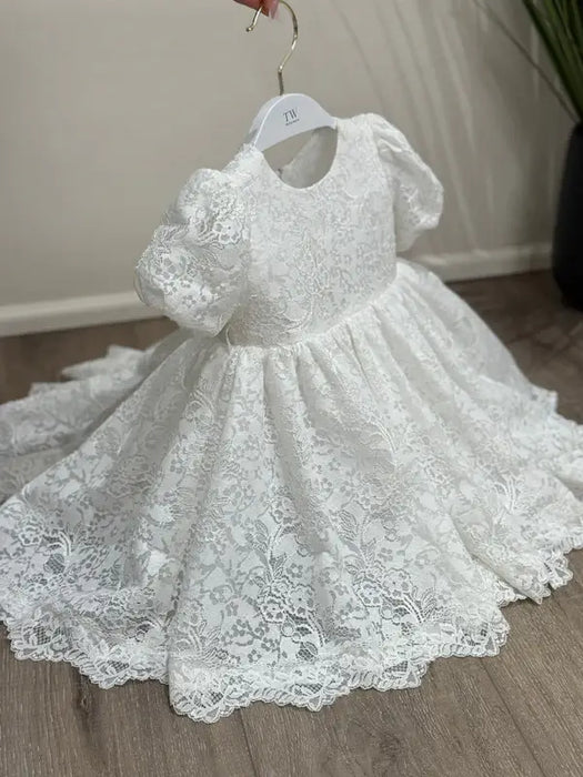 Precious Lace Baptism Dress white lace gown with puff sleeves shown on a hanger indoors.