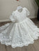 Precious Lace Baptism Dress white lace gown with puff sleeves shown on a hanger indoors.
