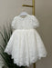 Warm Precious Lace Baptism Dress displayed on a hanger in a softly lit room.