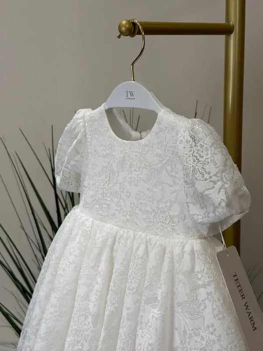 Teter Warm Precious Lace Baptism Dress with floral lace design displayed on a hanger indoors.