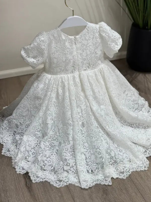 Precious Lace Baptism Dress white lace gown with short sleeves displayed on a hanger indoors.