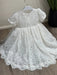 Precious Lace Baptism Dress white lace gown with short sleeves displayed on a hanger indoors.