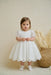 Precious Lace Baptism Dress shown on a toddler standing indoors near decorative wicker basket.