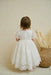 Precious Lace Baptism Dress shown on a toddler standing indoors near a wicker basket.