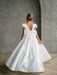 Teter Warm Quinn satin communion dress with large back bow shown on a girl in an elegant indoor setting.
