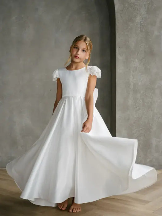 Teter Warm Quinn Satin Communion Dress shown on a young girl standing indoors, dress flowing elegantly.