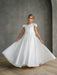 Quinn Satin Communion Dress shown on a young girl standing indoors, holding out the skirt.