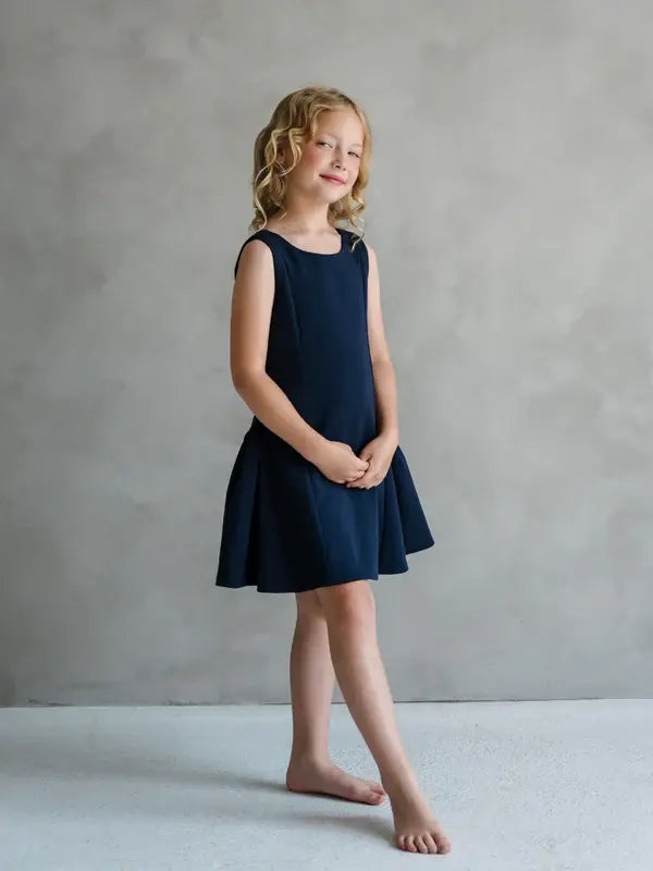 Teter Warm Rees dark sleeveless party dress worn by a young girl standing in a studio setting.