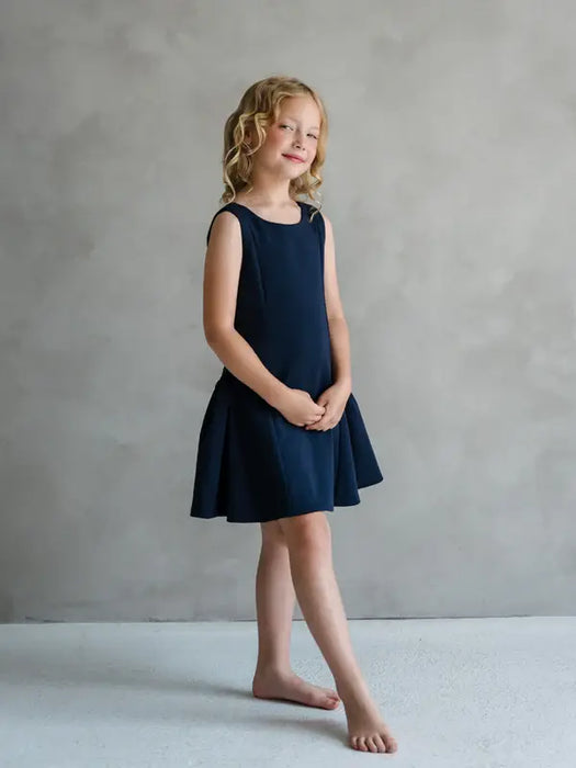 Teter Warm Rees dark sleeveless party dress worn by a young girl standing in a studio setting.