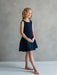 Teter Warm Rees dark sleeveless party dress worn by a young girl standing in a studio setting.