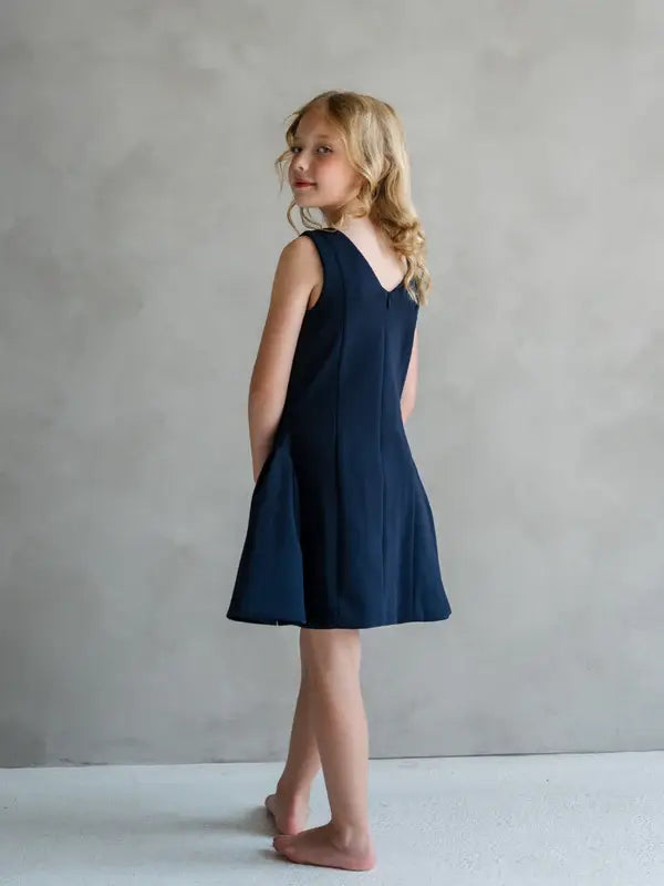 Teter Warm Rees dark sleeveless party dress shown on a young girl standing barefoot indoors.
