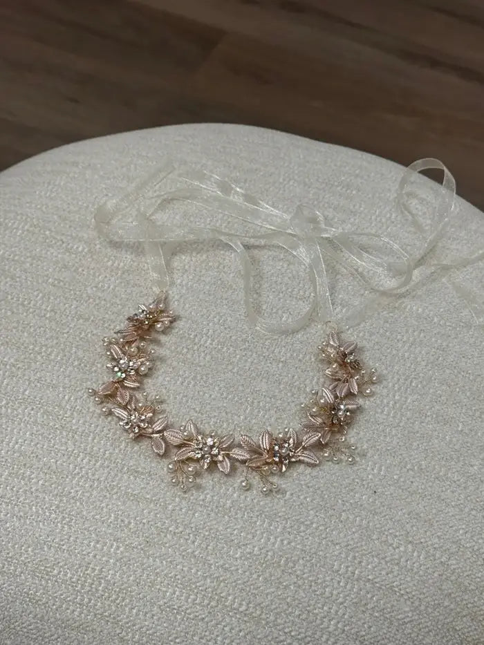 Teter Warm Renae rose gold rhinestone headpiece with floral design displayed on a beige fabric surface.