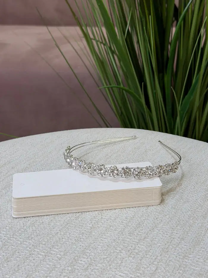 Teter Warm Rhinelline silver floral headpiece displayed on a textured surface with green plants in background.